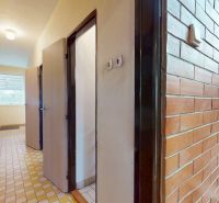 A hallway in a family house with brick cladding and wooden stairs leading to a window.