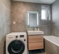 Bathroom in a 3-room apartment with a washing machine, sink, and bathtub, gray ceramic tiles.