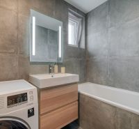 Bathroom in a 3-room apartment with a bathtub, sink, and washing machine; gray stone decor.