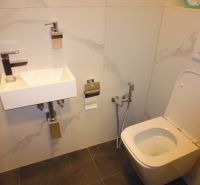 Bathroom with a toilet and a sink, tiled with light tiles.