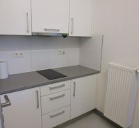 A small kitchen area with white cabinets, a gray countertop, and a radiator.