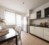 A kitchen in a 3-room apartment with a dining table, white cabinets, and a large window.