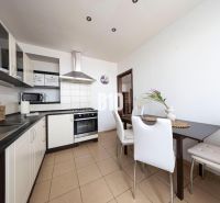 A kitchen in a 3-room apartment with white cabinets, a dining table, and appliances.
