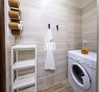 A bathroom with a washing machine and a shelving storage system in a three-room apartment.