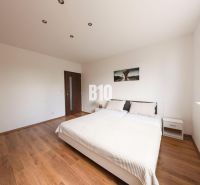 Bedroom with a double bed, wood-patterned flooring, and white walls in a three-room apartment.