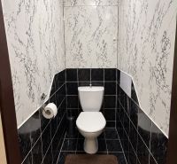 A toilet in a 3-room apartment with patterned walls and dark tiles.