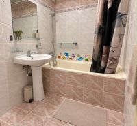 Bathroom in a three-room apartment with a bathtub, sink, large mirror, and tiles.