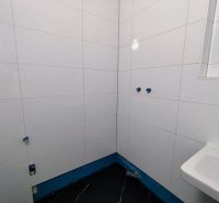 White tiles on the walls and a dark floor in the office bathrooms.