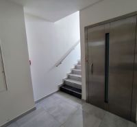Elevator and stairs in offices with white walls and tiles.