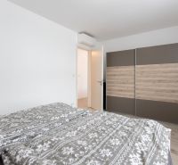 Bedroom in a 2-room apartment with white walls and a wardrobe with a wooden decor.
