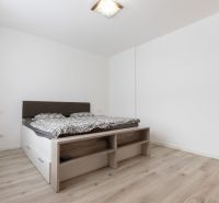 A bedroom with a bed, white walls, and a floor with a wooden decor in a 2-room apartment.
