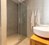 Bathroom in a 2-room apartment with a washing machine, shower, and sinks on wood decor.