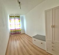 A bright room with a wood-patterned floor in a three-room apartment, a white wardrobe, colorful curtains.