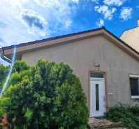 A family house in Matúškovo with white doors, surrounded by greenery under a sunny sky.