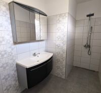 A bathroom with white tiles and a shower enclosure, without a shower tray, in a family house.
