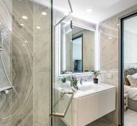 A bathroom with a glass shower enclosure, marble walls, and a white sink in a vacation apartment.