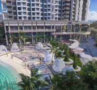 A recreational apartment in Jomtien by the pool with palm trees and sunbeds on the sand.