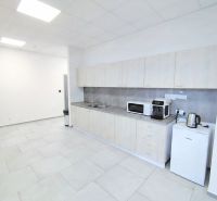 Offices with a bright kitchenette, cabinets, microwave oven, and refrigerator, with tiles on the floor.