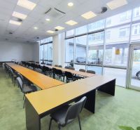Commercial spaces with large windows, long tables and chairs, green carpet.