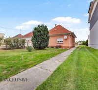 A family house in Povoda surrounded by lawn and trees, a concrete path leads to the house.