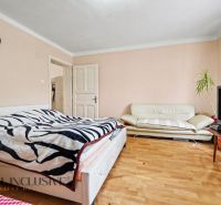 Bedroom with a bed, couch, television, and wooden decor flooring in a family house.