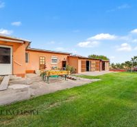 A family house in Povoda with a garden, wooden seating, and a garage in the background.