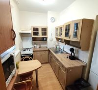 A kitchen in a studio apartment with a wooden decor floor, table, chairs, appliances.