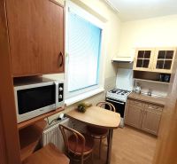 A kitchen in a studio apartment with a wooden decor floor, includes a table, microwave, and stove.
