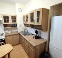 A kitchen in a studio apartment with a wooden decor floor and spacious cabinets.