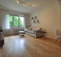 Living room in a two-room apartment with a sofa, large windows, and a wooden decor floor.