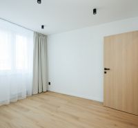 An empty room with a wood-patterned floor and a window with curtains in a two-room apartment.