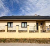 A family house in Nickelsdorf with a white facade and a black roof behind a fence.