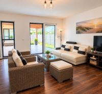 A bright living room with wood-patterned flooring, white sofas, and rattan furniture.
