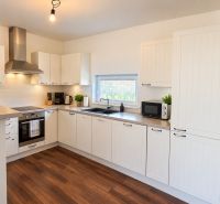 A kitchen in a family house with a wooden decor floor and white cabinets.