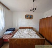 A bedroom in a family house with wooden wardrobes and a bed, delicate curtains on the window.