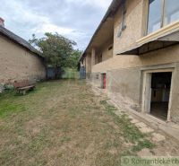 The courtyard of a family house in Nižné Ladičkovce with a bench and lawn, next to a stone wall.