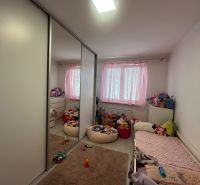 A room in a 3-room apartment with pink curtains, a wardrobe, and children's toys on the floor.