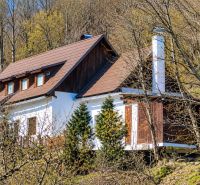 A cottage in Banská Štiavnica surrounded by forest, steep roof, wooden accents.