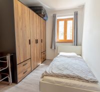 A small room in a family house with a bed, a built-in wardrobe, and a window with curtains.