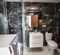 A bathroom in a family house with a washing machine, black marble walls, and a shower enclosure.