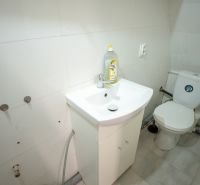 A bathroom in a family house with a sink and a toilet, simple white tiles.