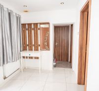 A hallway in a family house with white walls, curtains, and wooden doors.