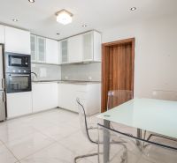 A kitchen in a family house with a glass table, cabinets, and appliances, flooring with a white decor.