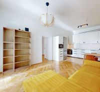 Living room of a four-room apartment with a wooden decor floor, a yellow sofa, and a kitchenette.