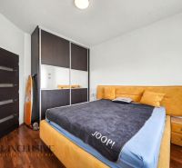 A bedroom in a family house with a bed, built-in wardrobe, and wooden decor flooring.