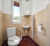 Bathroom with toilet and sink in a family house, beige tiles, white window.