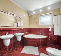 A bathroom in a family house with a corner bathtub and two sinks, red tiles.