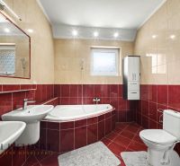 A bathroom in a family house with a corner bathtub, red and beige tiles.