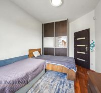 A bedroom with two beds and a built-in wardrobe in a family house with a wooden decor floor.