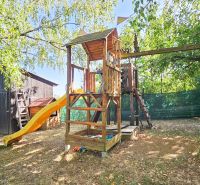 A wooden swing with a slide near the cottage surrounded by greenery in Suchá nad Parnou.